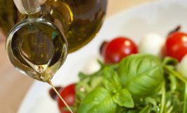 Pouring olive oil salad dressing onto tomato, mozarella and rocket salad with basil garnish and balsamic vinegar